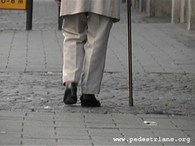 Pedestrian with cane negotiating cobblestones.